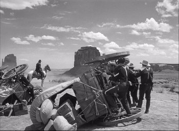 Movie still from “Fort Apache” (1948), directed by John Ford – A black and white photo of a group of men standing around a pile of luggage; Wide shot, Low angle