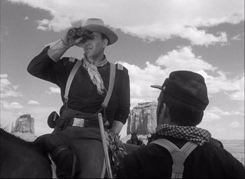 Movie still from “Fort Apache” (1948), directed by John Ford – A man on a horse looking through binoculars at another man; Medium shot, Low angle