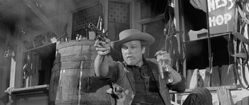 Movie still from “Forty Guns” (1957), directed by Samuel Fuller – A man in a cowboy hat holding a gun and a beer; Medium shot, Low angle