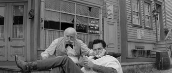 Movie still from “Forty Guns” (1957), directed by Samuel Fuller – Two men sitting in front of a building one shaving the other's beard; Medium shot, Over the shoulder angle