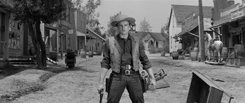 Movie still from “Forty Guns” (1957), directed by Samuel Fuller – A man in a cowboy hat holding a gun in the middle of a dirt road; Medium shot, Low angle