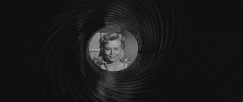 Movie still from “Forty Guns” (1957), directed by Samuel Fuller – A black and white photo of a woman looking through a hole in the wall; Close Up shot, Low angle