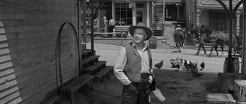 Movie still from “Forty Guns” (1957), directed by Samuel Fuller – An old man in a hat and a vest standing in front of a building; Medium shot, Over the shoulder angle