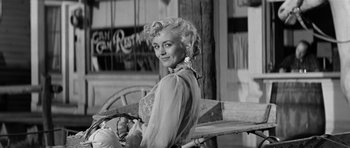 Movie still from “Forty Guns” (1957), directed by Samuel Fuller – A black - and - white photo of a woman sitting on top of a bench; Medium shot, Low angle