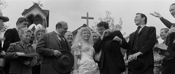 Movie still from “Forty Guns” (1957), directed by Samuel Fuller – A group of people standing around a woman in front of a cross; Medium shot, Low angle