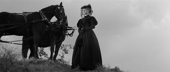Movie still from “Forty Guns” (1957), directed by Samuel Fuller – A woman standing next to a horse on top of a hill; Wide shot, Low angle