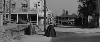Movie still from “Forty Guns” (1957), directed by Samuel Fuller – A woman in a black dress standing next to a pole; Wide shot, Low angle