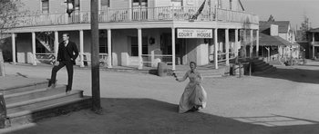Movie still from “Forty Guns” (1957), directed by Samuel Fuller – An old photo of a woman holding a gun in front of a court house; Wide shot, Low angle