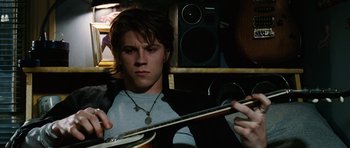 Movie still from “Four Brothers” (2005), directed by John Singleton – A young man holding a guitar while sitting in a room; Medium shot, Low angle