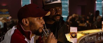Movie still from “Four Brothers” (2005), directed by John Singleton – Two men are sitting at a table and one of them is drinking a beverage; Close Up shot, Over the shoulder angle