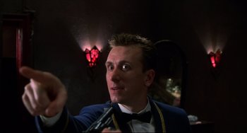 Movie still from “Four Rooms” (1995), directed by Robert Rodriguez – A man in a suit and bow tie holding a microphone; Close Up shot, Low angle