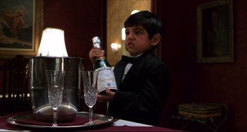 Movie still from “Four Rooms” (1995), directed by Robert Rodriguez – A young boy in a tuxedo holding a bottle of champagne; Medium shot, Low angle
