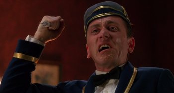 Movie still from “Four Rooms” (1995), directed by Robert Rodriguez – A man in a blue uniform is holding his fist up in the air; Close Up shot, Low angle