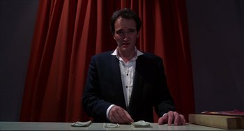 Movie still from “Four Rooms” (1995), directed by Robert Rodriguez – A man in a black suit and white shirt is playing a card game; Medium shot, Low angle