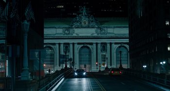 Movie still from “The Upside” (2017), directed by Neil Burger – A car driving down a street in front of a large building; Extreme Wide shot, High angle