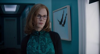 Movie still from “The Upside” (2017), directed by Neil Burger – A woman with glasses standing in front of a picture of a bird; Medium shot, Low angle