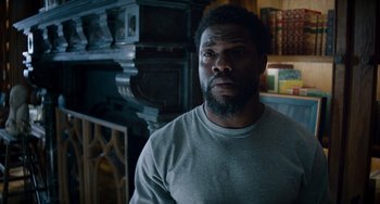 Movie still from “The Upside” (2017), directed by Neil Burger – A man with a beard is standing in front of a fireplace; Close Up shot, Over the shoulder angle