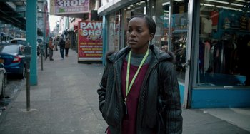 Movie still from “The Upside” (2017), directed by Neil Burger – A woman standing on the sidewalk wearing a black jacket; Medium shot, Over the shoulder angle