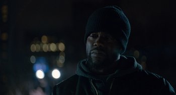 Movie still from “The Upside” (2017), directed by Neil Burger – A man with a beard wearing a black hat; Close Up shot, Over the shoulder angle