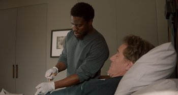 Movie still from “The Upside” (2017), directed by Neil Burger – A man in a hospital bed with a man in white gloves; Medium shot, Overhead angle