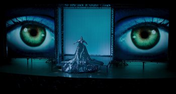 Movie still from “The Upside” (2017), directed by Neil Burger – A woman in a silver dress standing on a stage; Extreme Wide shot, Overhead angle