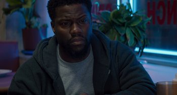 Movie still from “The Upside” (2017), directed by Neil Burger – A person sitting in a room near a plant; Close Up shot, Over the shoulder angle