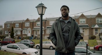 Movie still from “The Upside” (2017), directed by Neil Burger – A man standing next to a lamp post on a city street; Medium shot, Low angle
