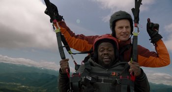 Movie still from “The Upside” (2017), directed by Neil Burger – A man holding a ski pole while riding on the back of another man; Medium shot, Overhead angle