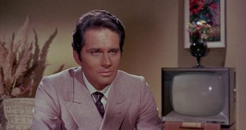 Movie still from “Four Times That Night” (1971), directed by Mario Bava – A man in a suit and tie sitting in front of a tv; Close Up shot, Over the shoulder angle