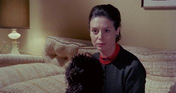Movie still from “Four Times That Night” (1971), directed by Mario Bava – A woman in a black shirt and red necklace holding a stuffed animal; Close Up shot, Over the shoulder angle