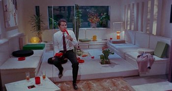 Movie still from “Four Times That Night” (1971), directed by Mario Bava – A man sitting on the ground holding a red object; Wide shot, High angle