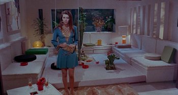 Movie still from “Four Times That Night” (1971), directed by Mario Bava – A woman in a blue dress standing in front of a living room; Wide shot, High angle