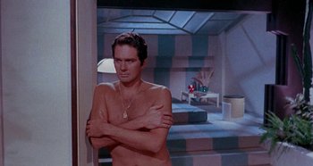 Movie still from “Four Times That Night” (1971), directed by Mario Bava – A man with his arms crossed standing in front of a mirror; Medium shot, High angle