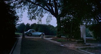 Movie still from “Four Times That Night” (1971), directed by Mario Bava – A car parked on the side of the road under a large tree; Extreme Wide shot, High angle