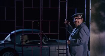 Movie still from “Four Times That Night” (1971), directed by Mario Bava – A man standing next to a metal fence; Medium shot, Low angle