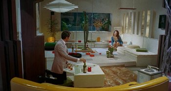 Movie still from “Four Times That Night” (1971), directed by Mario Bava – A man and a woman are sitting in a living room; Wide shot, High angle