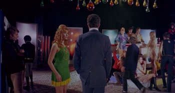 Movie still from “Four Times That Night” (1971), directed by Mario Bava – A man and a woman are standing in front of other people; Wide shot, Over the shoulder angle
