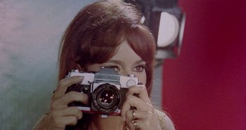 Movie still from “Four Times That Night” (1971), directed by Mario Bava – A woman taking a picture of herself with a camera; Close Up shot, Low angle