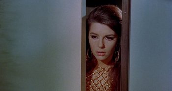 Movie still from “Four Times That Night” (1971), directed by Mario Bava – A beautiful woman in a gold dress standing in a doorway; Close Up shot, High angle