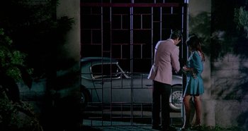 Movie still from “Four Times That Night” (1971), directed by Mario Bava – A man in a pink jacket standing in front of a car; Wide shot, High angle