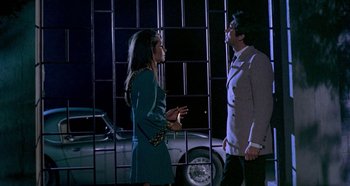 Movie still from “Four Times That Night” (1971), directed by Mario Bava – A man and a woman standing next to each other in front of a car; Medium shot, Low angle