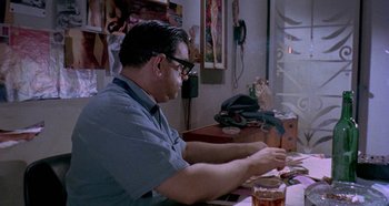 Movie still from “Four Times That Night” (1971), directed by Mario Bava – A man sitting at a table in front of a glass of beer; Medium shot, Low angle