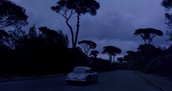 Movie still from “Four Times That Night” (1971), directed by Mario Bava – A car driving down a road near a forest at night; Extreme Wide shot, Low angle