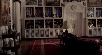 Movie still from “Foxcatcher” (2014), directed by Bennett Miller – A man sitting in front of a bookcase filled with trophies; Wide shot, High angle