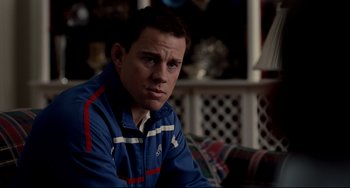Movie still from “Foxcatcher” (2014), directed by Bennett Miller – A man in a blue jacket sitting on a couch; Close Up shot, Over the shoulder angle