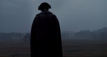 Movie still from “Foxcatcher” (2014), directed by Bennett Miller – A man in a black coat and a hat standing in the middle of a field; Wide shot, Low angle