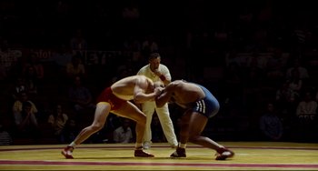 Movie still from “Foxcatcher” (2014), directed by Bennett Miller – Two men wrestling in front of an audience; Wide shot, High angle