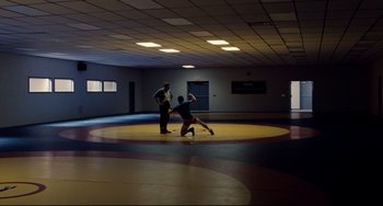 Movie still from “Foxcatcher” (2014), directed by Bennett Miller – Two men in a wrestling ring one is throwing a ball; Extreme Wide shot, Low angle