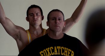 Movie still from “Foxcatcher” (2014), directed by Bennett Miller – Two men standing next to each other in front of a white wall; Medium shot, Low angle