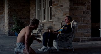 Movie still from “Foxcatcher” (2014), directed by Bennett Miller – A man sitting in a chair talking to another man; Wide shot, Over the shoulder angle